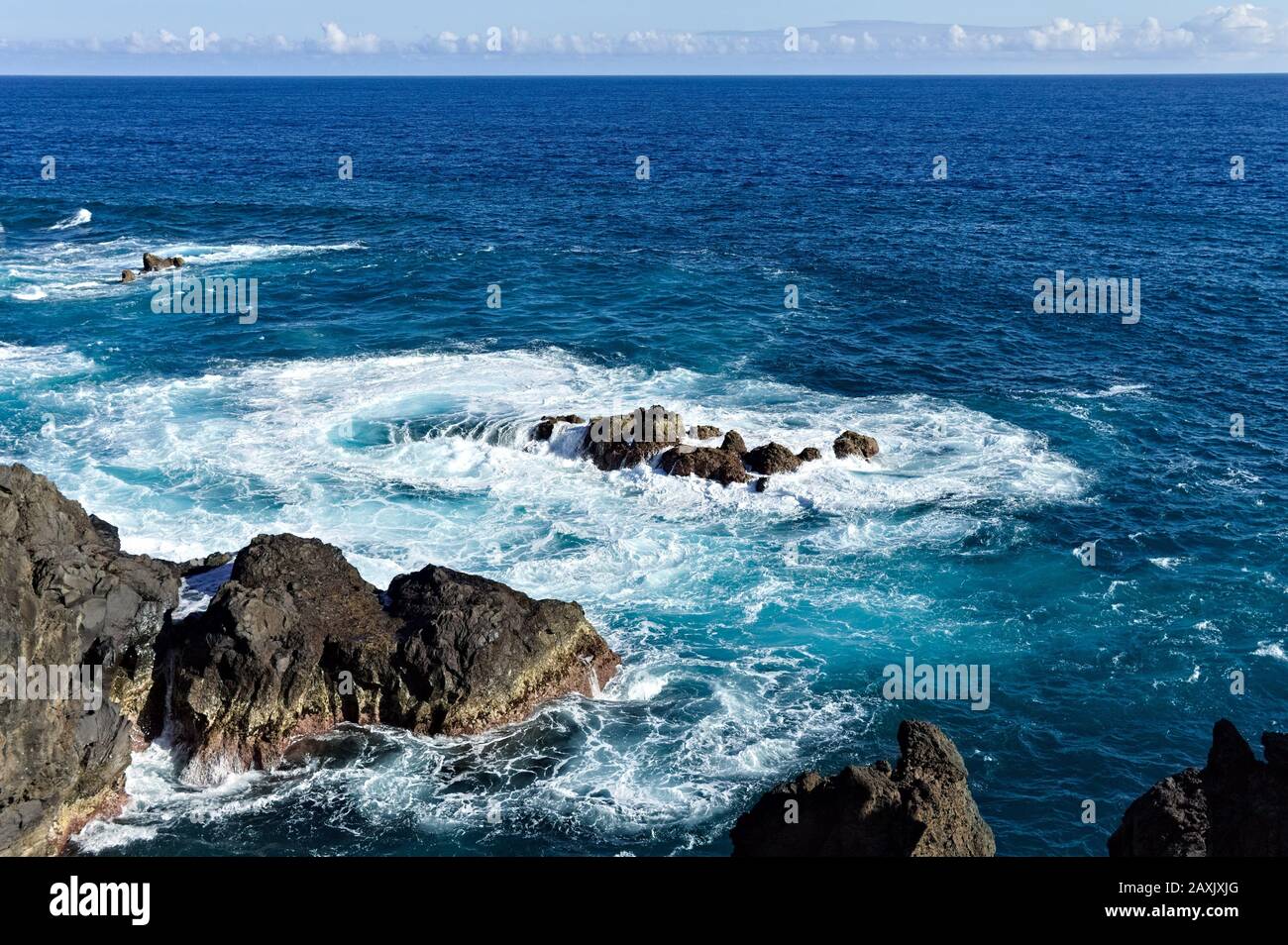 White foam of the waves crashing on the volcanic rock groynes in the ...