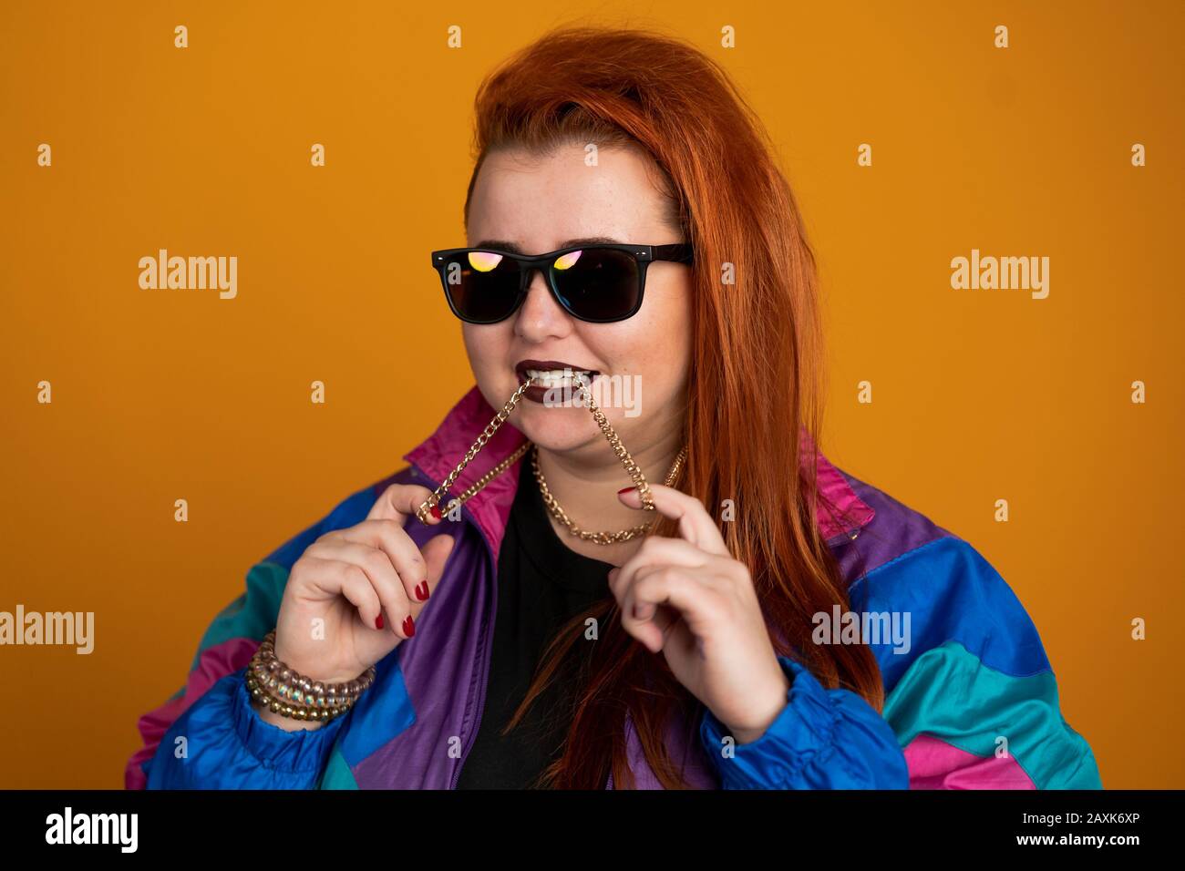 Red haired woman in sunglasses biting chain isolated on yellow ...
