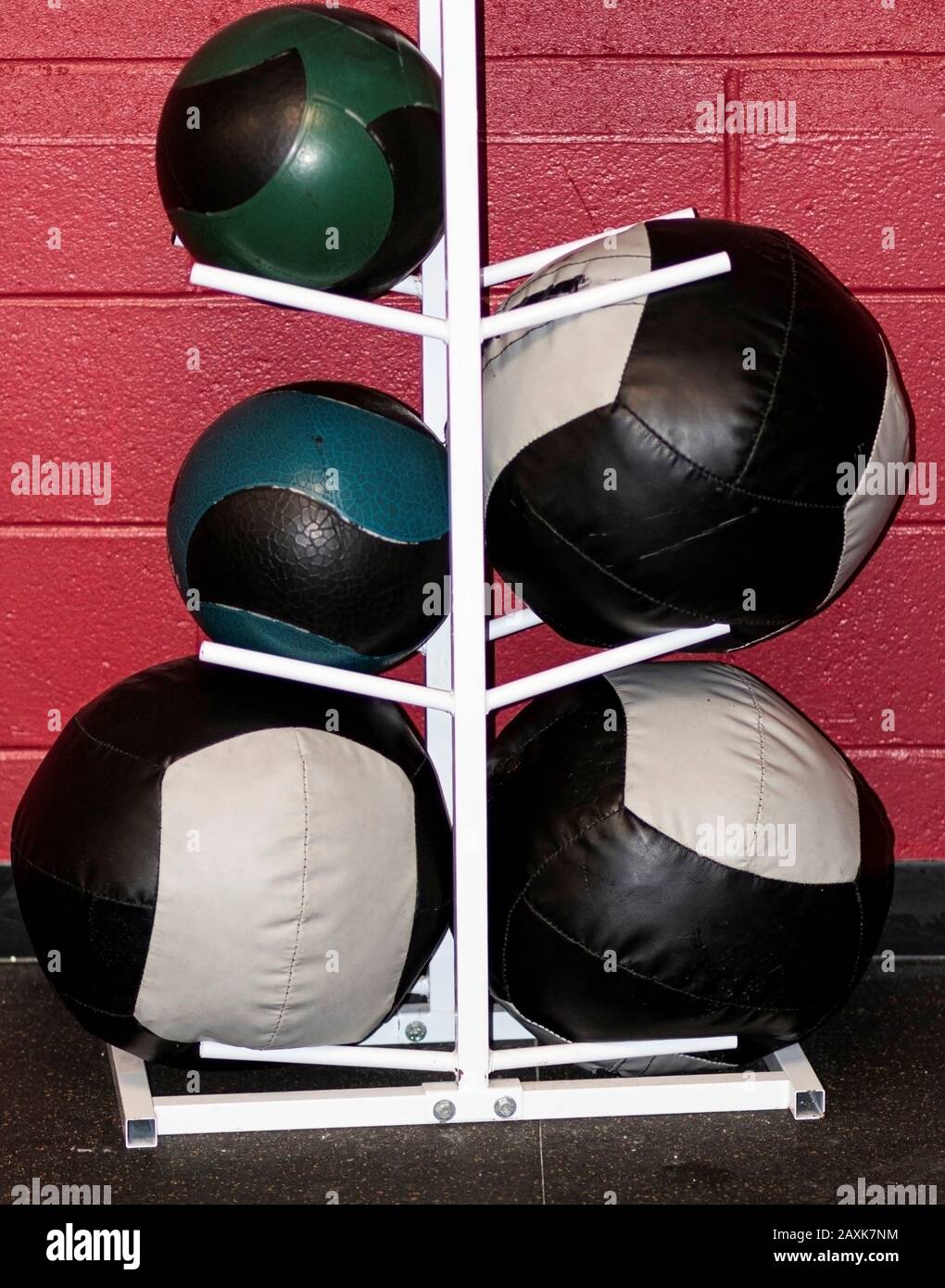 Different sizes of medicine balls on a white rack against a red wall inside a gym. Stock Photo