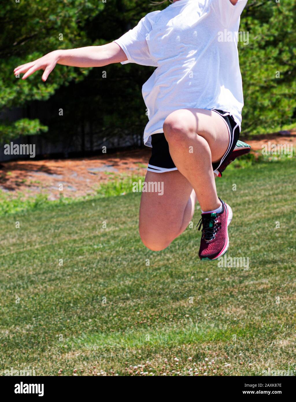 A high school girl is jumping high in the air practicing long and triple jump during track and field practice. Stock Photo