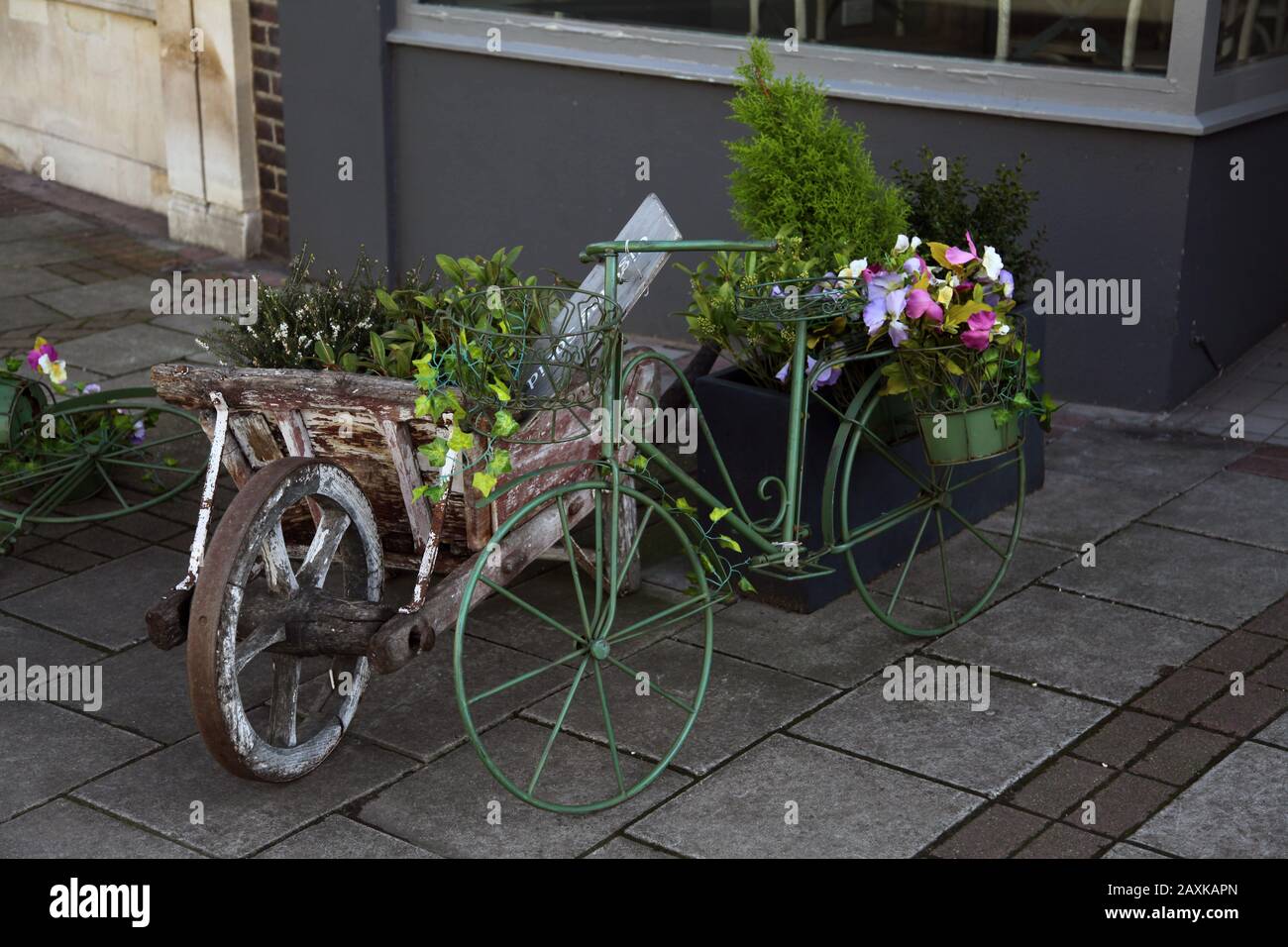 Interesting flower display in old wooden wheelbarrow and bicycle frame on High Street, Esher, Surrey, UK Stock Photo