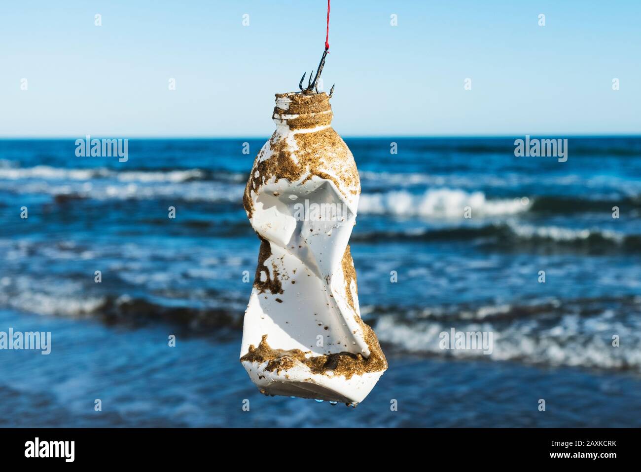 closeup of a used plastic bottle, covered with wet sand, in a fish hook, freshly fished in the ocean, in front of the water Stock Photo