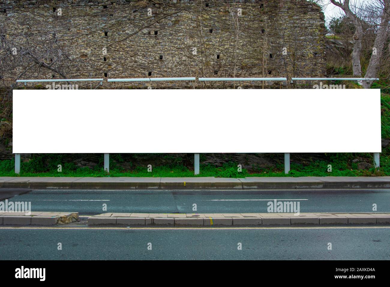 Blank billboard at the roadside photographed from the opposite sidewalk, with an old castle in the background Stock Photo