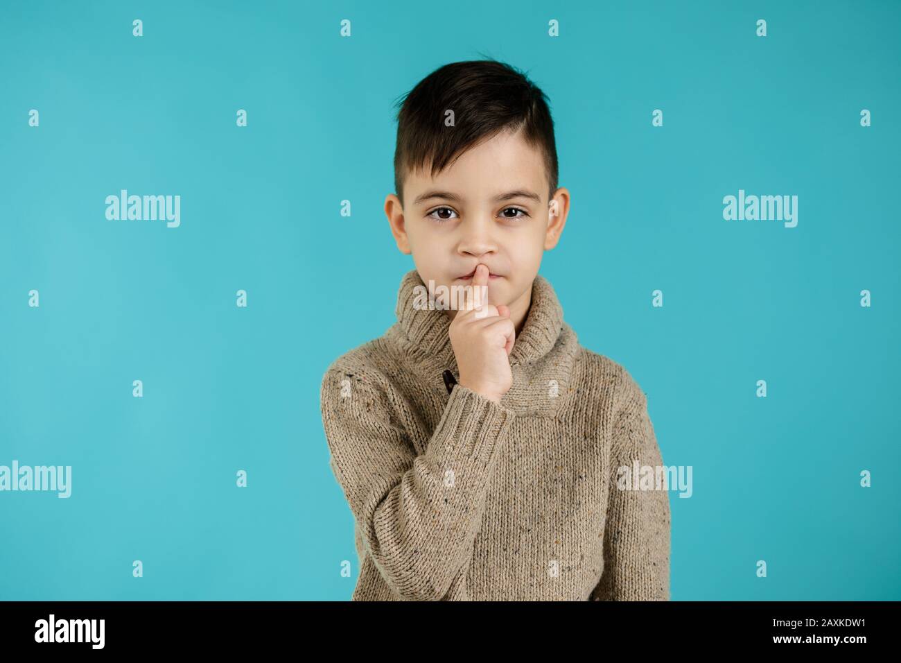 cute little boy asking to be quiet with finger on lips on blue