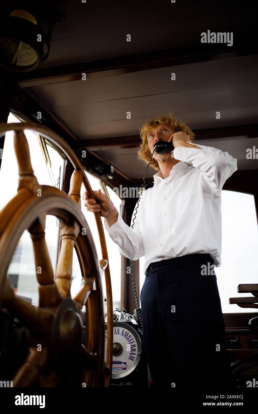 Captain steering a vintage boat standing behind a wooden wheel Stock