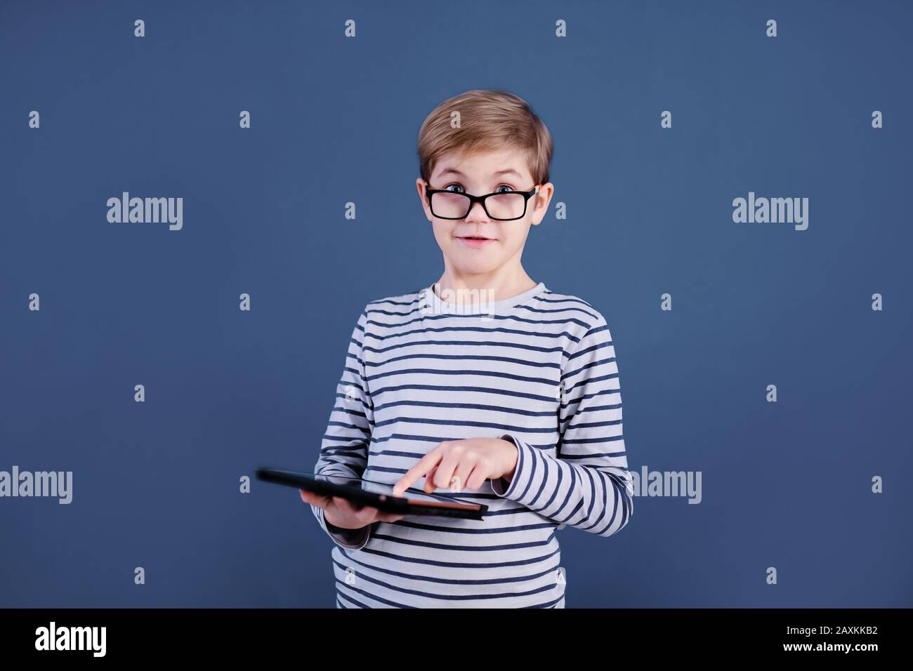 Blonde child boy with big glasses playing with tablet pc on blue  background. Education concept Stock Photo - Alamy