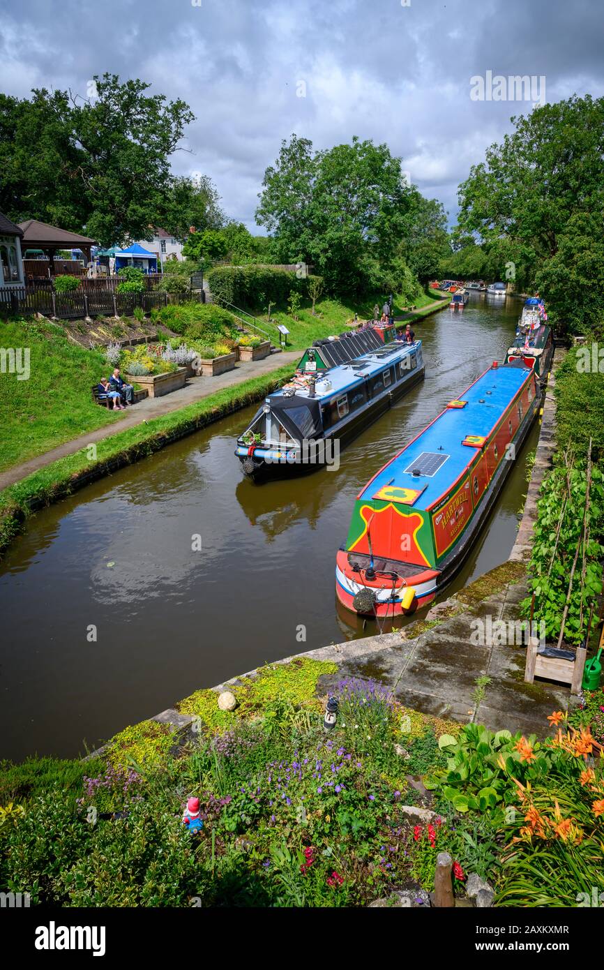 Looking down from a bridge over the canal on a boat passing moored narrowboats at the Gnosall Canal Festival in the Staffordshire UK village. Stock Photo