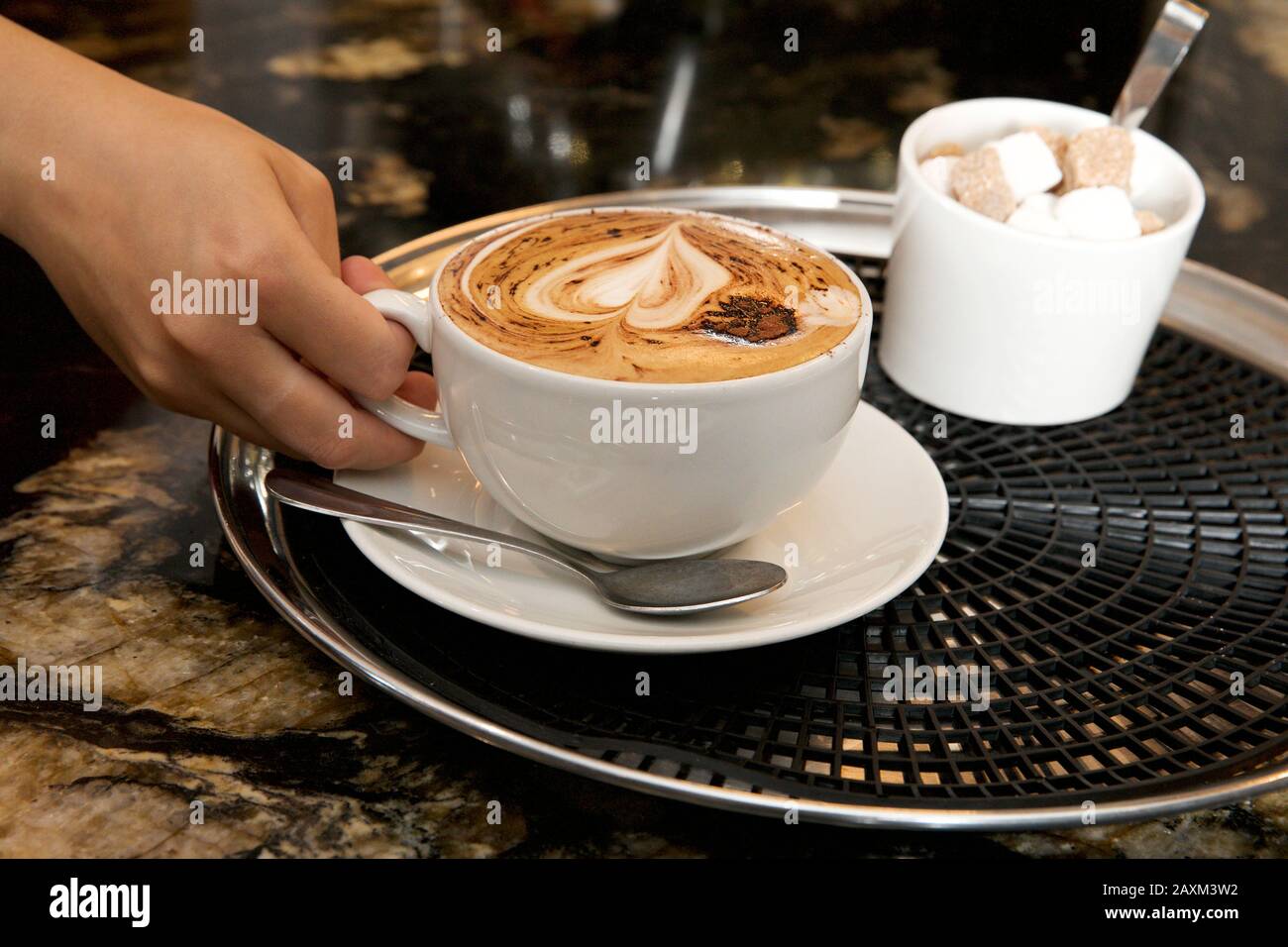 A woman's hand about to lift a cup of cappuccino coffee. Stock Photo
