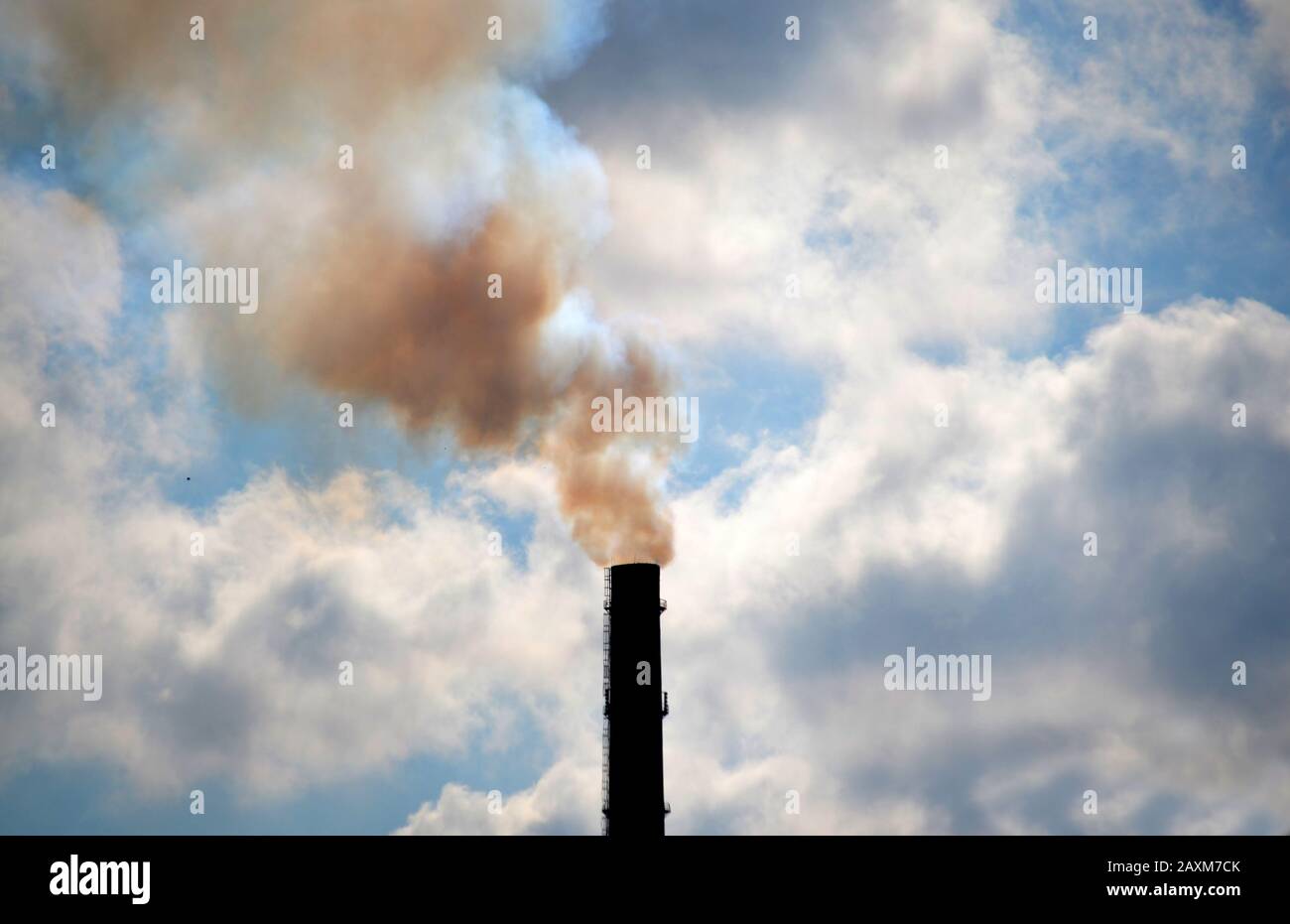 technogenic contrasting background tip of the black silhouette pipe with smoke sky with bright clouds and sun backlight Stock Photo