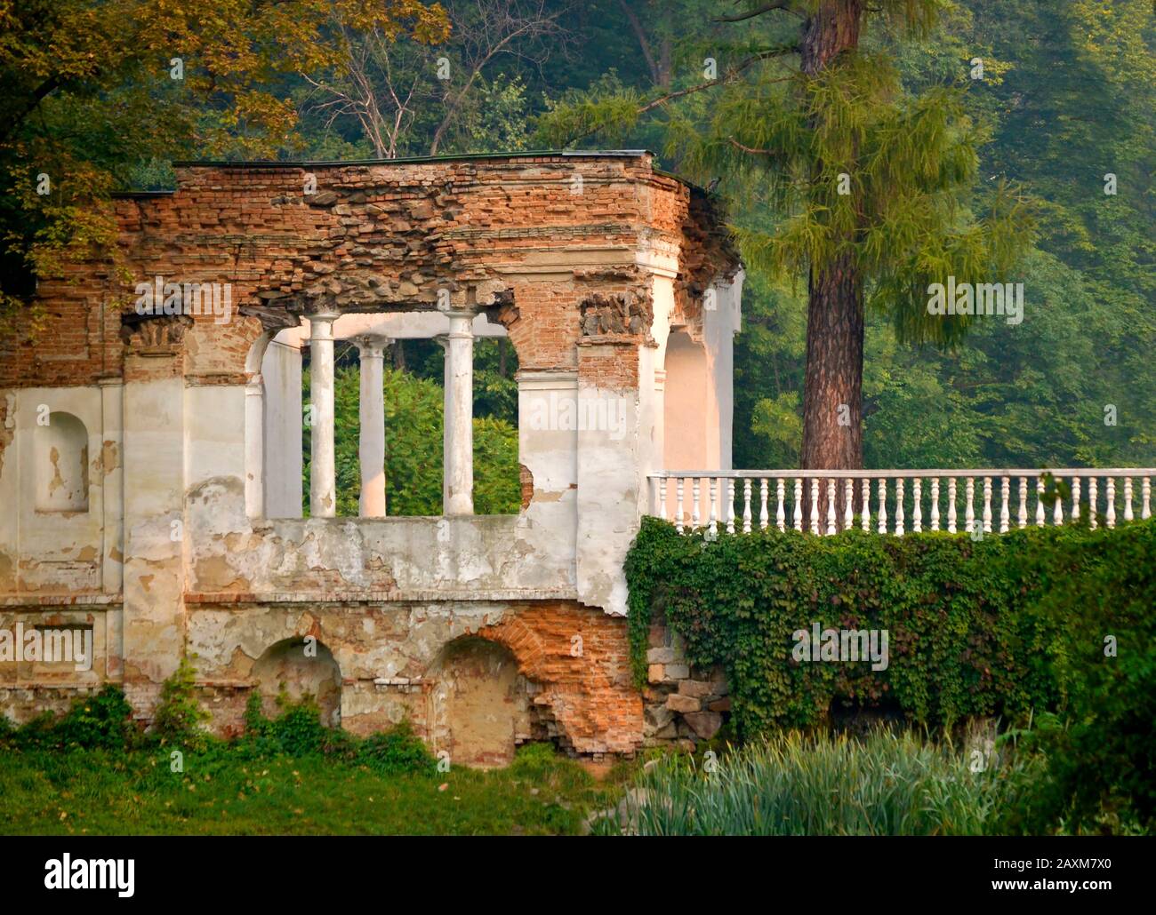 Ruins of red brick with white railing with columns and plaster in the park with green trees in the background Stock Photo