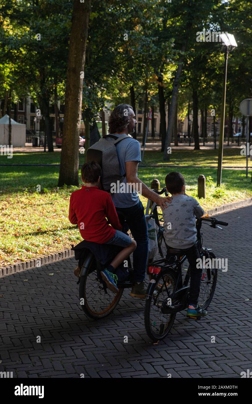 Ein Mann und zwei Jungen radeln gemächlich durch Den Haag, die niederländische Hauptstadt. // A man and two young boys cycling leisurely through The H Stock Photo