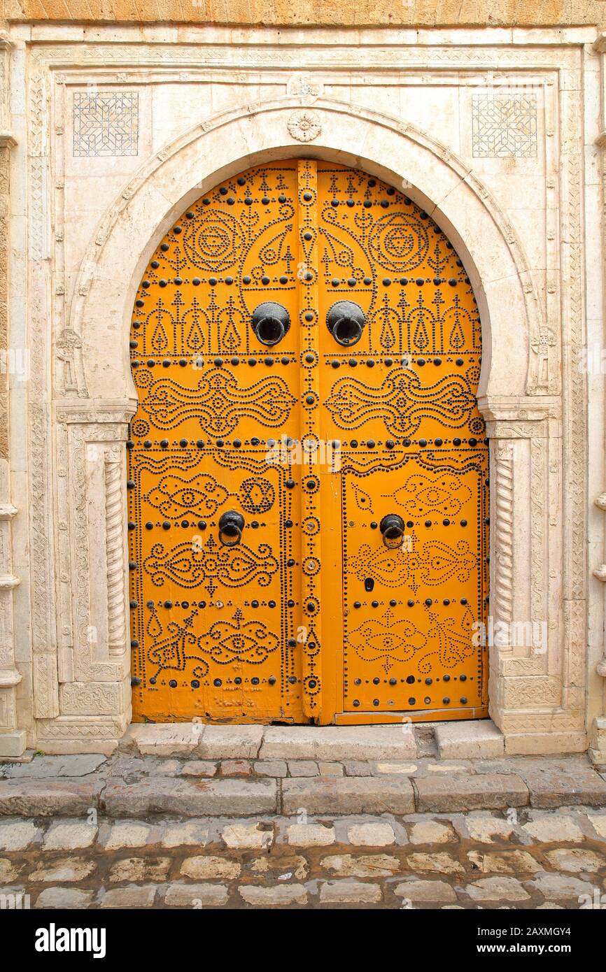 A traditional ornate wooden door inside the medina of Tunis, Tunisia, with traditional knockers and walls with carvings Stock Photo