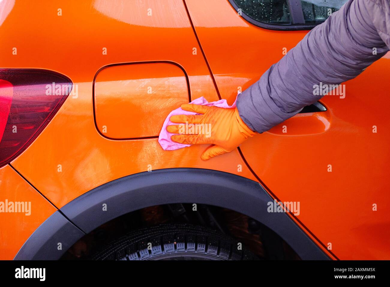 Man after cleaning wipes his orange car with a pink rag  at car wash. Male hand and car body closeup. Stock Photo