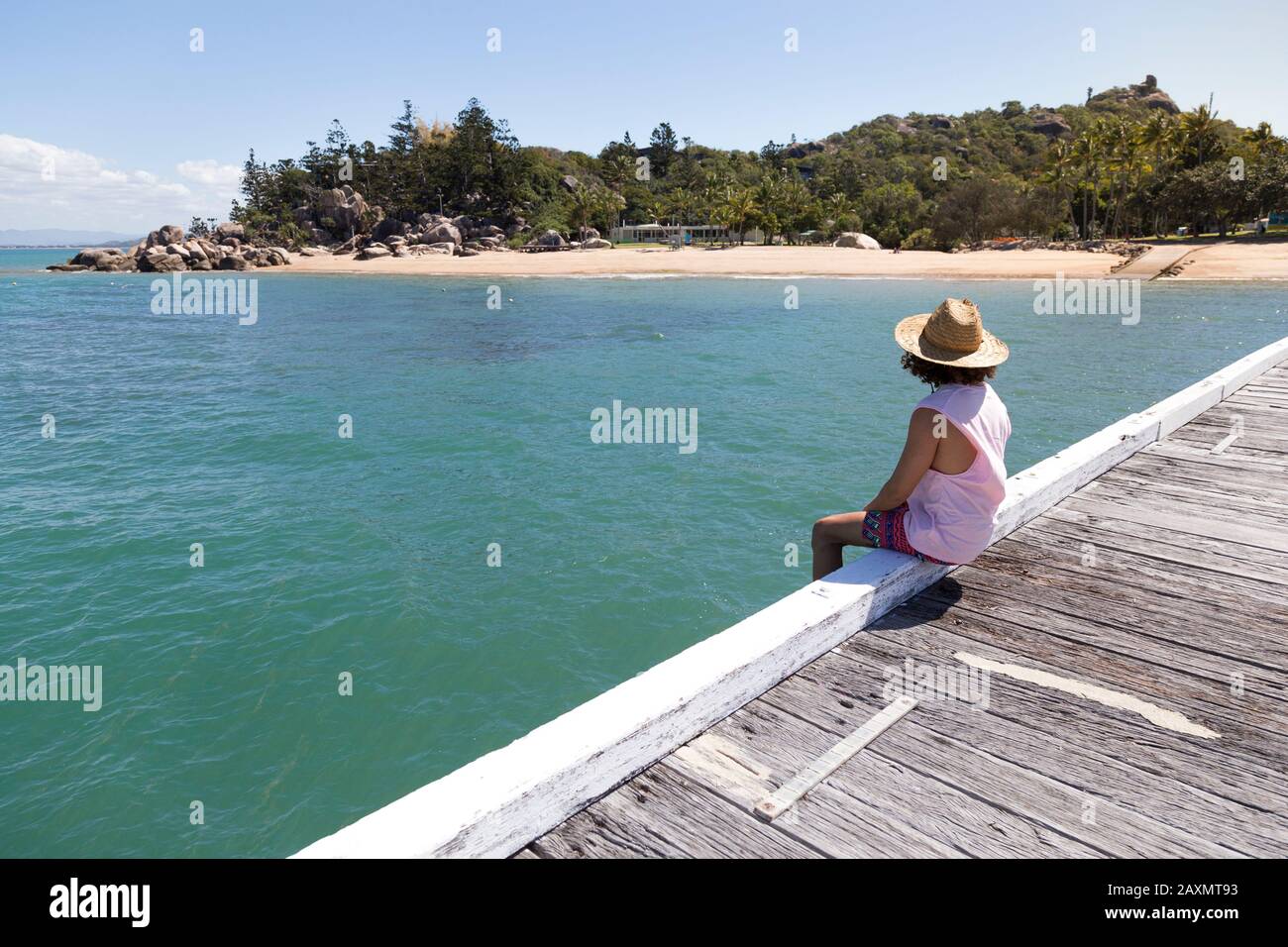 Curly hair man, with sun hat, sitted on edge of wooden dock Stock Photo