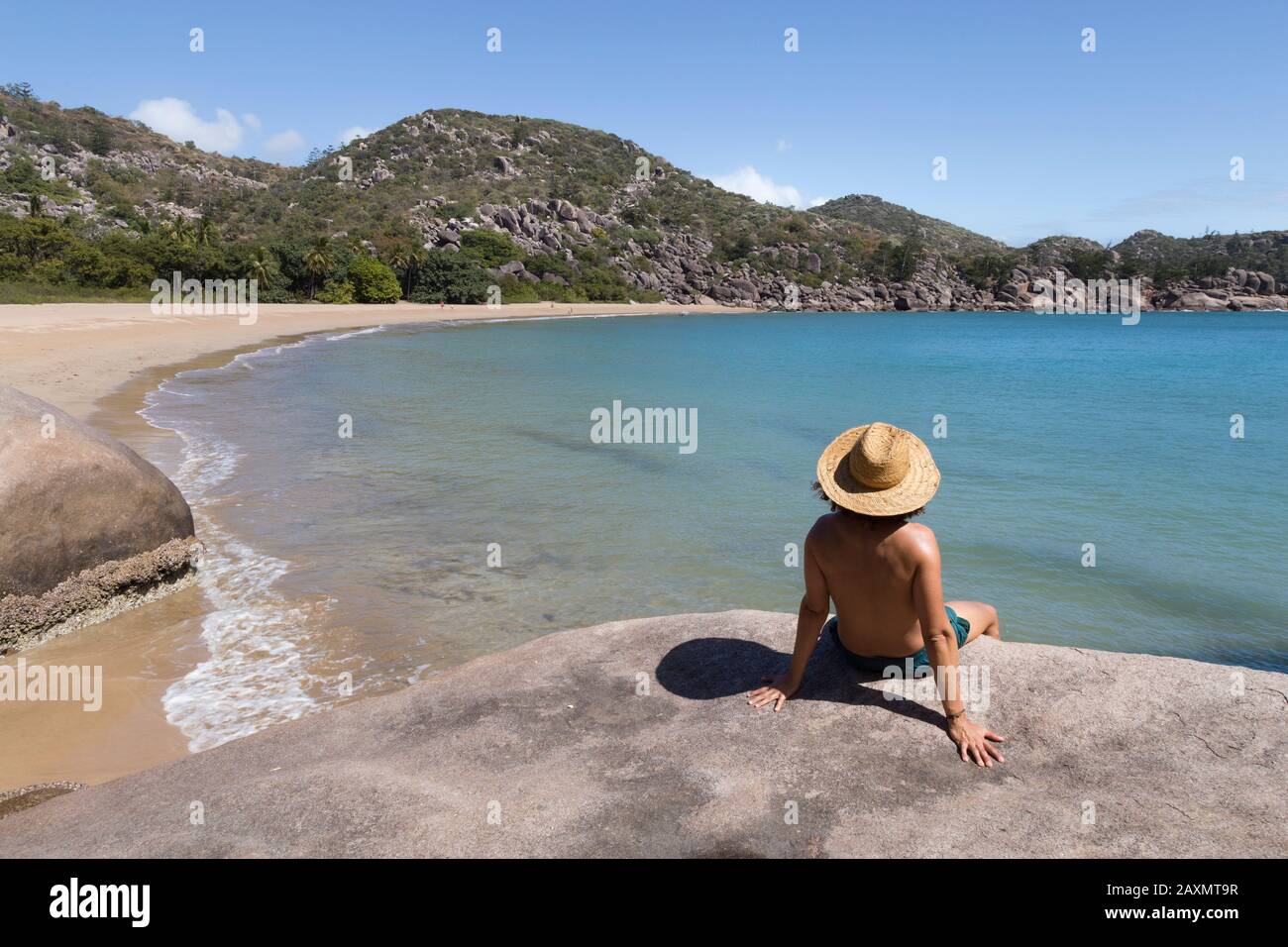 Curly hair man with hat and swimsuit, on top of rock, admiring the bay Stock Photo