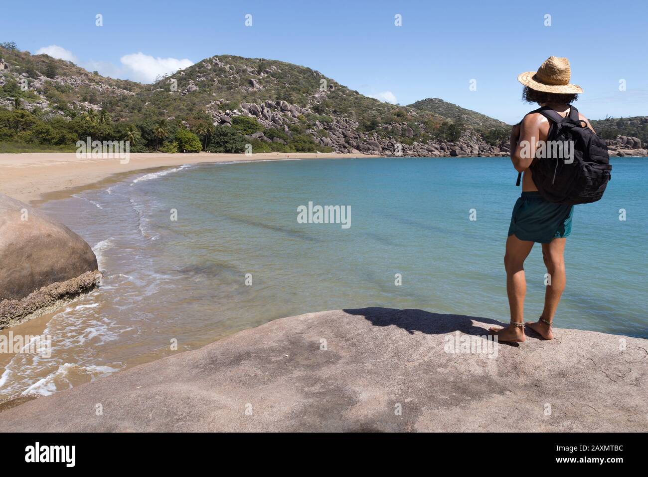 Backpacker with hat and swimsuit, on top of rock, admiring the bay Stock Photo
