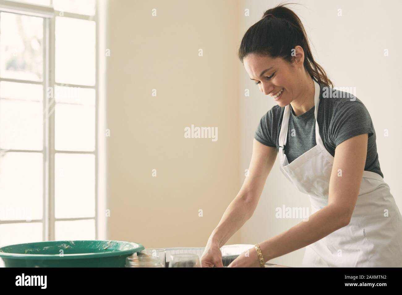Smiling woman wearing apron while preparing food on table against wall at home Stock Photo
