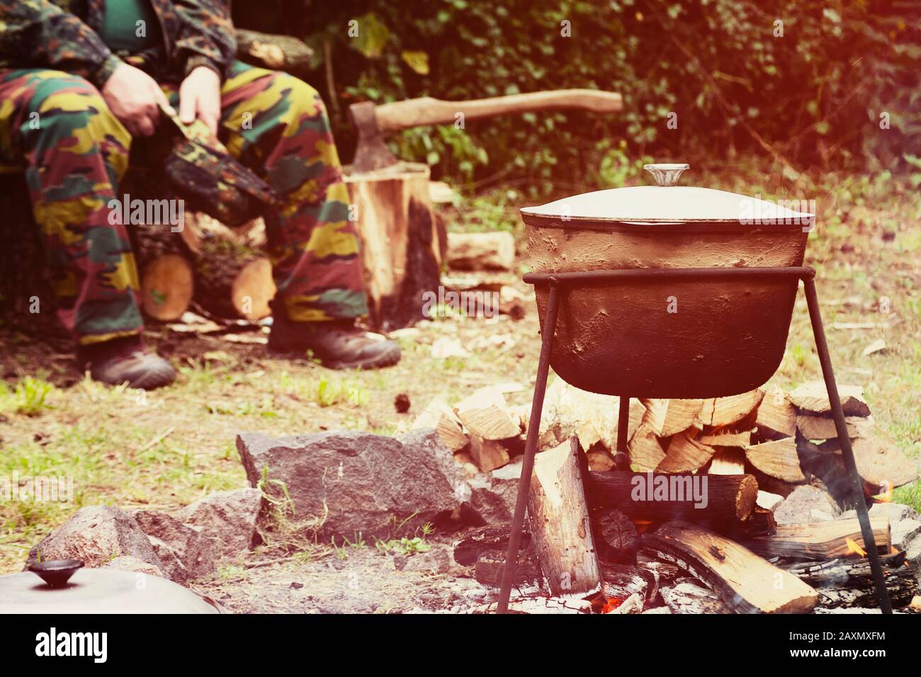 man in camouflage sitting in a forest near the camp-pot on the fire Stock Photo