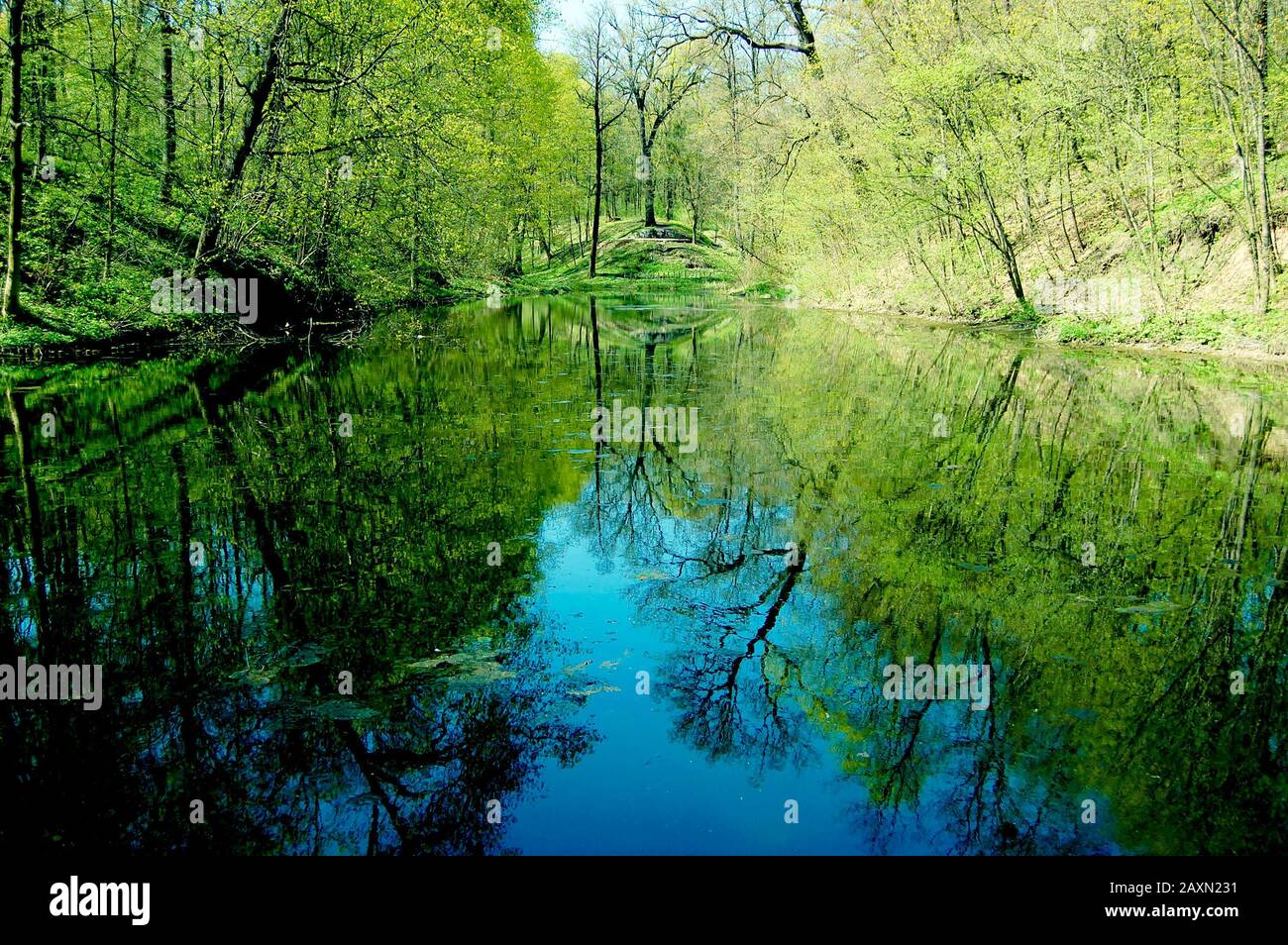 blue water lake in the spring park, on the banks of trees and reflected in the calm water, blue-green filter Stock Photo