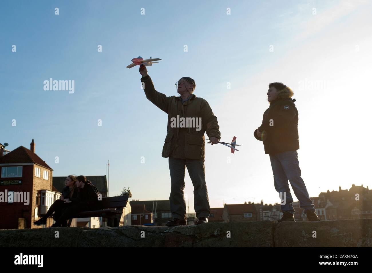 83 year old grandfather and teenage grandson flying paper planes together off Tate Hill pier in Whitby, North Yorkshire, UK. Stock Photo