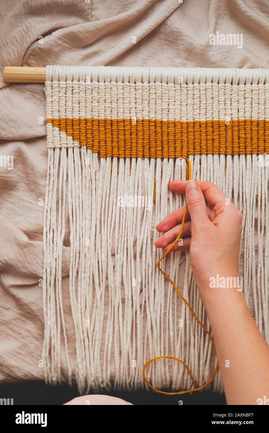 Handcrafted macrame wall hanging, close-up view. Human hand making a piece of decor Stock Photo