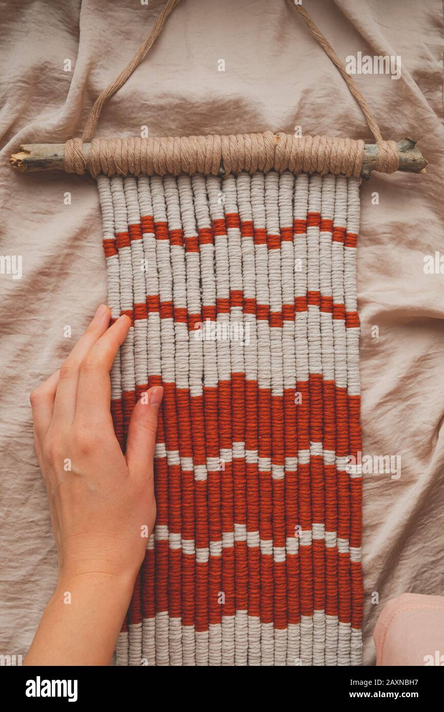 Handcrafted macrame wall hanging, close-up view. Human hand touches a handcrafted piece of decor Stock Photo