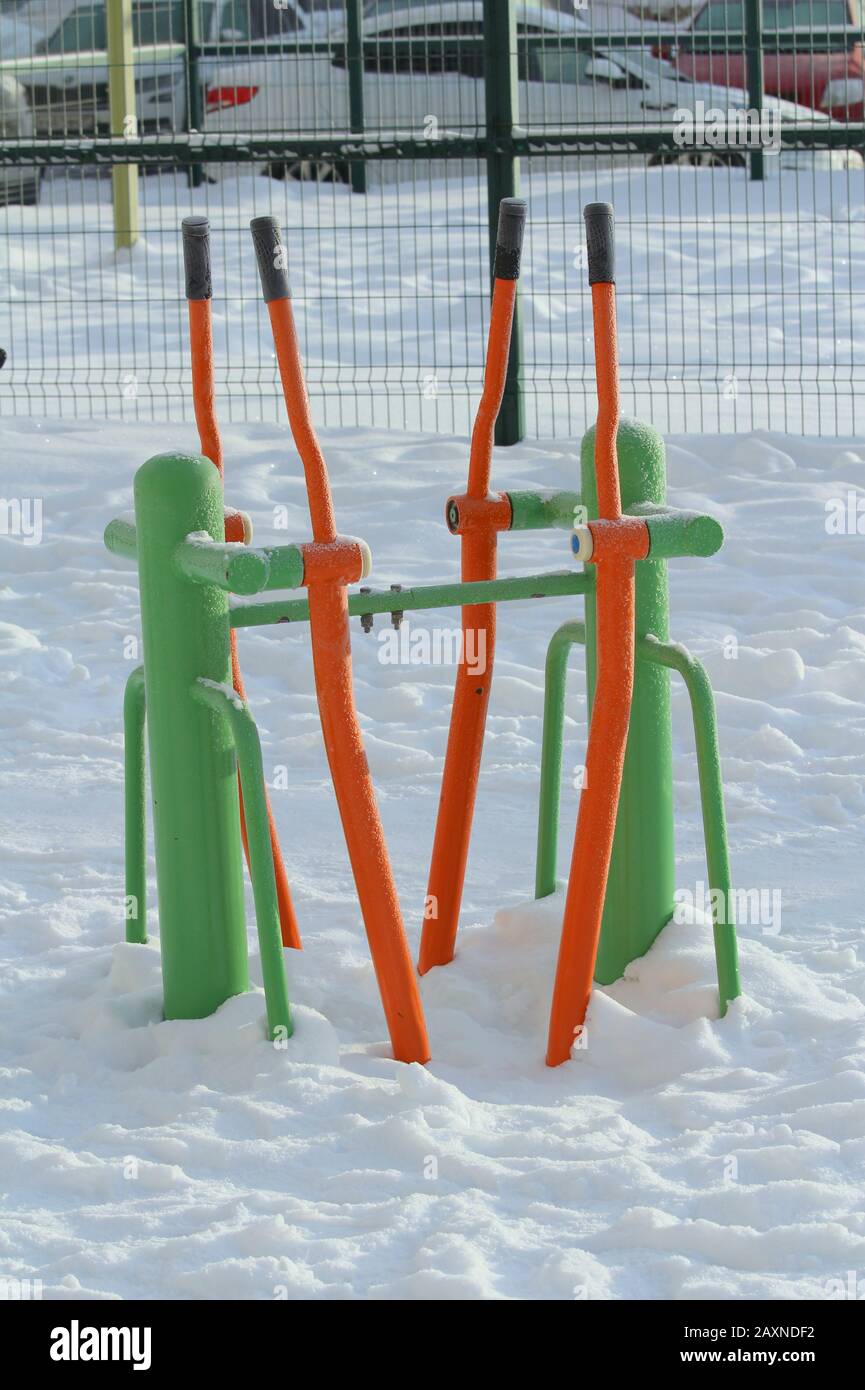 Outdoor fitness equipment on winter urban background, concept of active winter recreation, health care. Vibrant cheerful greens and oranges color. Stock photo with empty space for text. Stock Photo