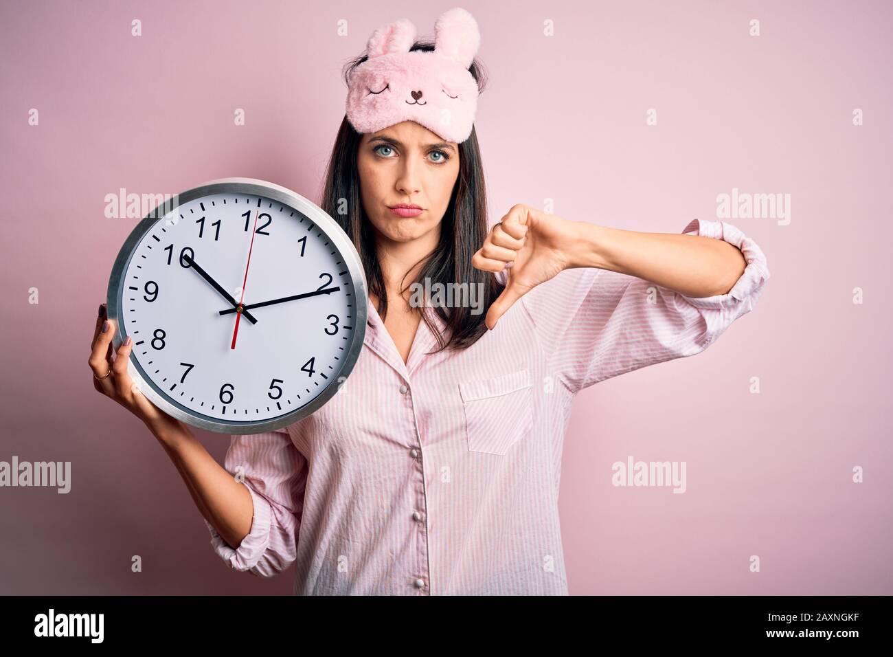 Young brunette woman with blue eyes wearing pajama holding big clock at ...