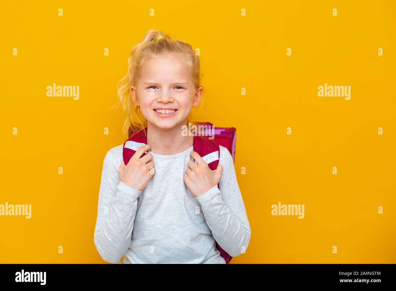 Back to school. Portrait of blonde caucasian school girl with bag on yellow studio background. Education. looking and smiling at camera. Stock Photo