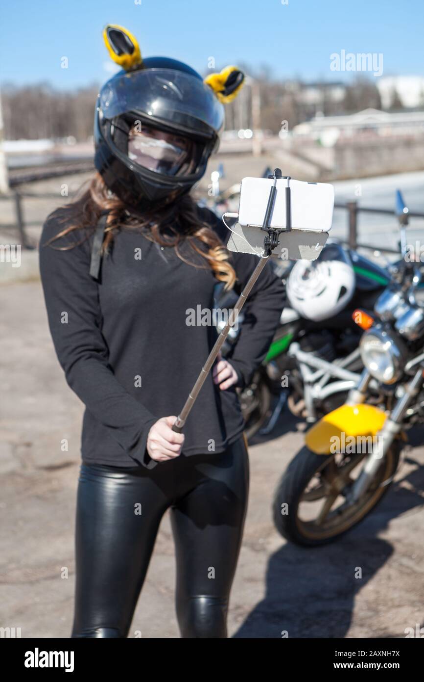 Young Caucasian woman motorcyclist take selfies using cellphone with extensible monopod Stock Photo