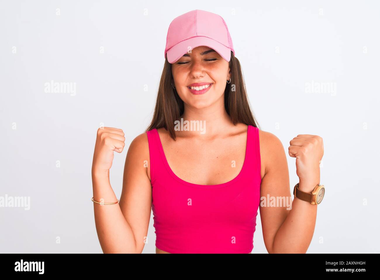 Young beautiful girl wearing pink casual t-shirt and cap over isolated white background very happy and excited doing winner gesture with arms raised, Stock Photo