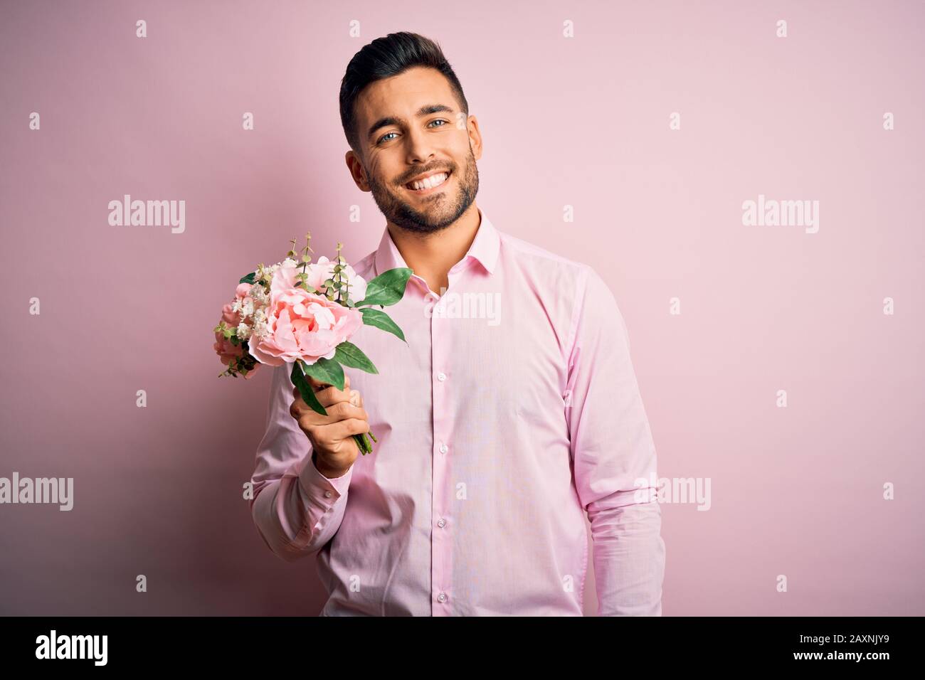 Young romatic man holding bouquet of spring flowers over pink isolatd ...
