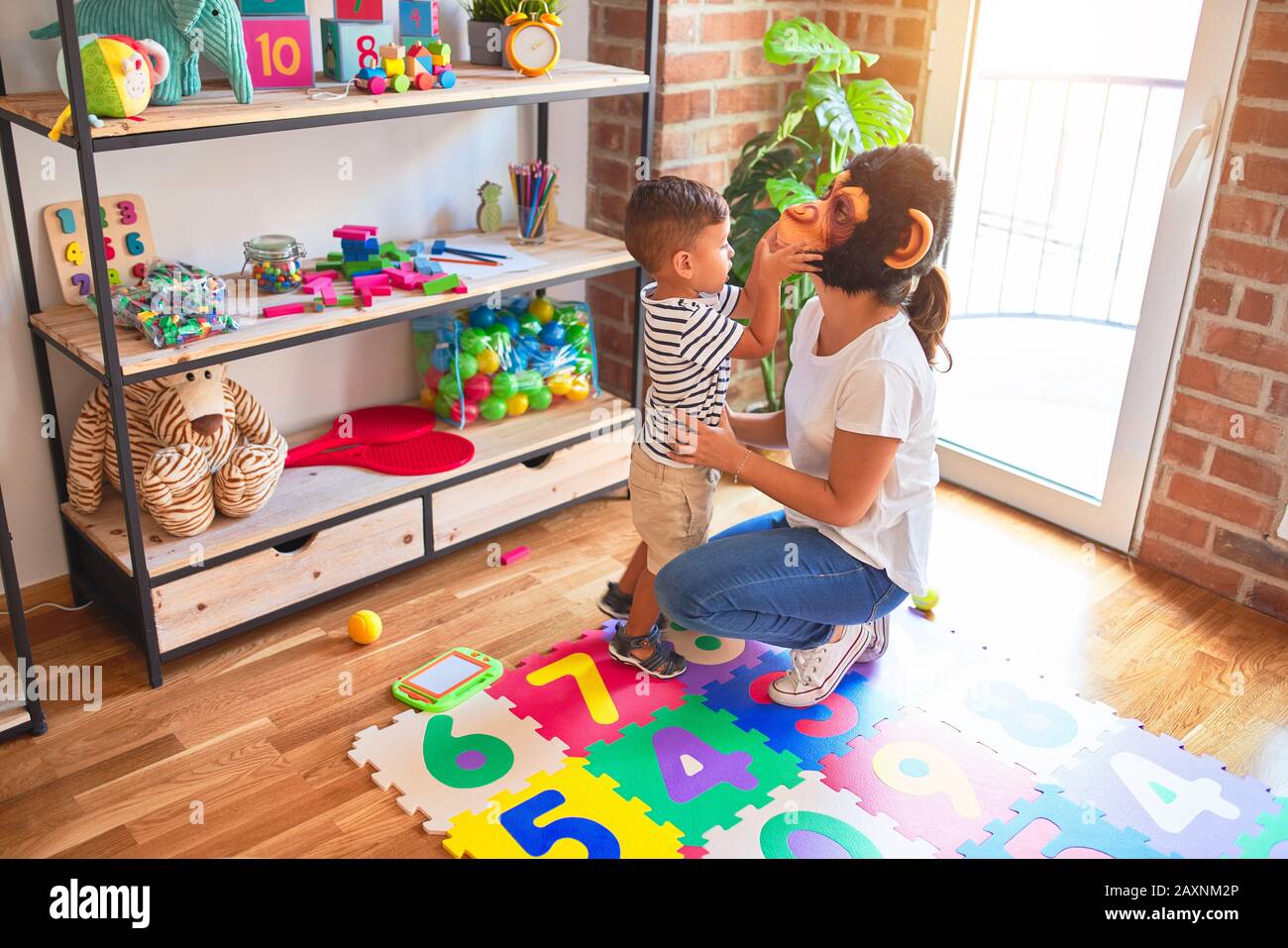 Beautiful teacher and toddler boy playing, woman with monkey mask at kindergarten Stock Photo