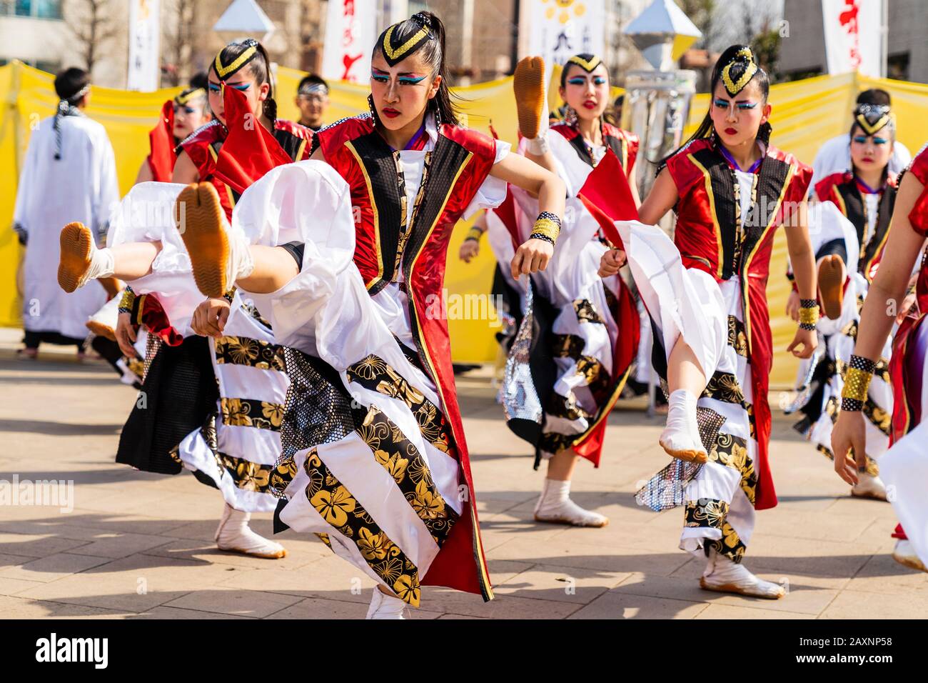 Japanese Yosakoi dance group dancing in public square at the Kyusyu Gassai festival in Kumamoto. Women dancers in red happi coats kicking legs up. Stock Photo