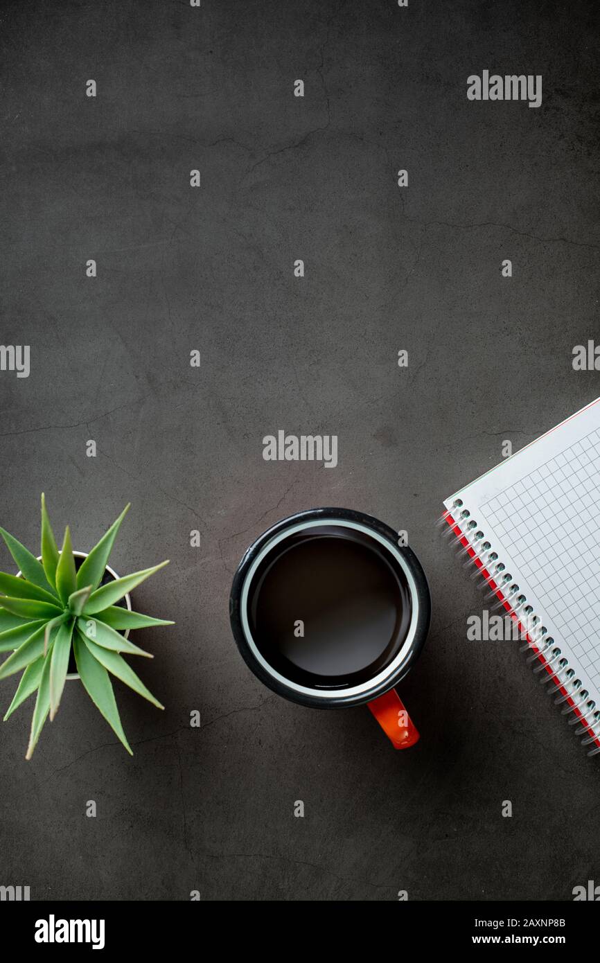 table top view with notepad, coffee and plant on black background. Stock Photo
