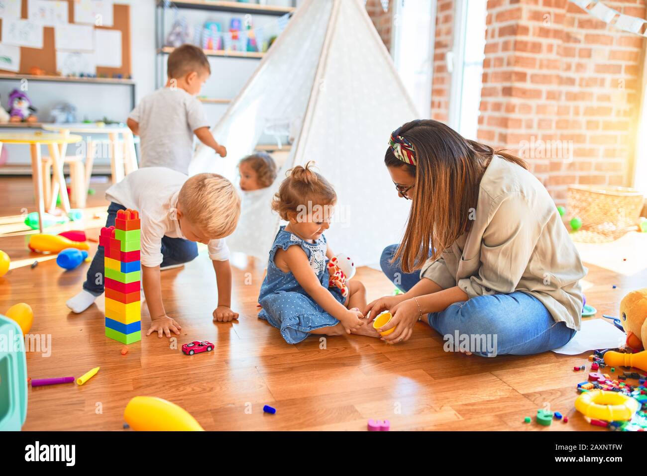 Beautiful teacher and group of toddlers playing around lots of toys at