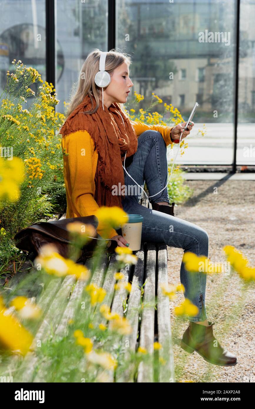 Young woman sits in front of office building and hears music Stock Photo