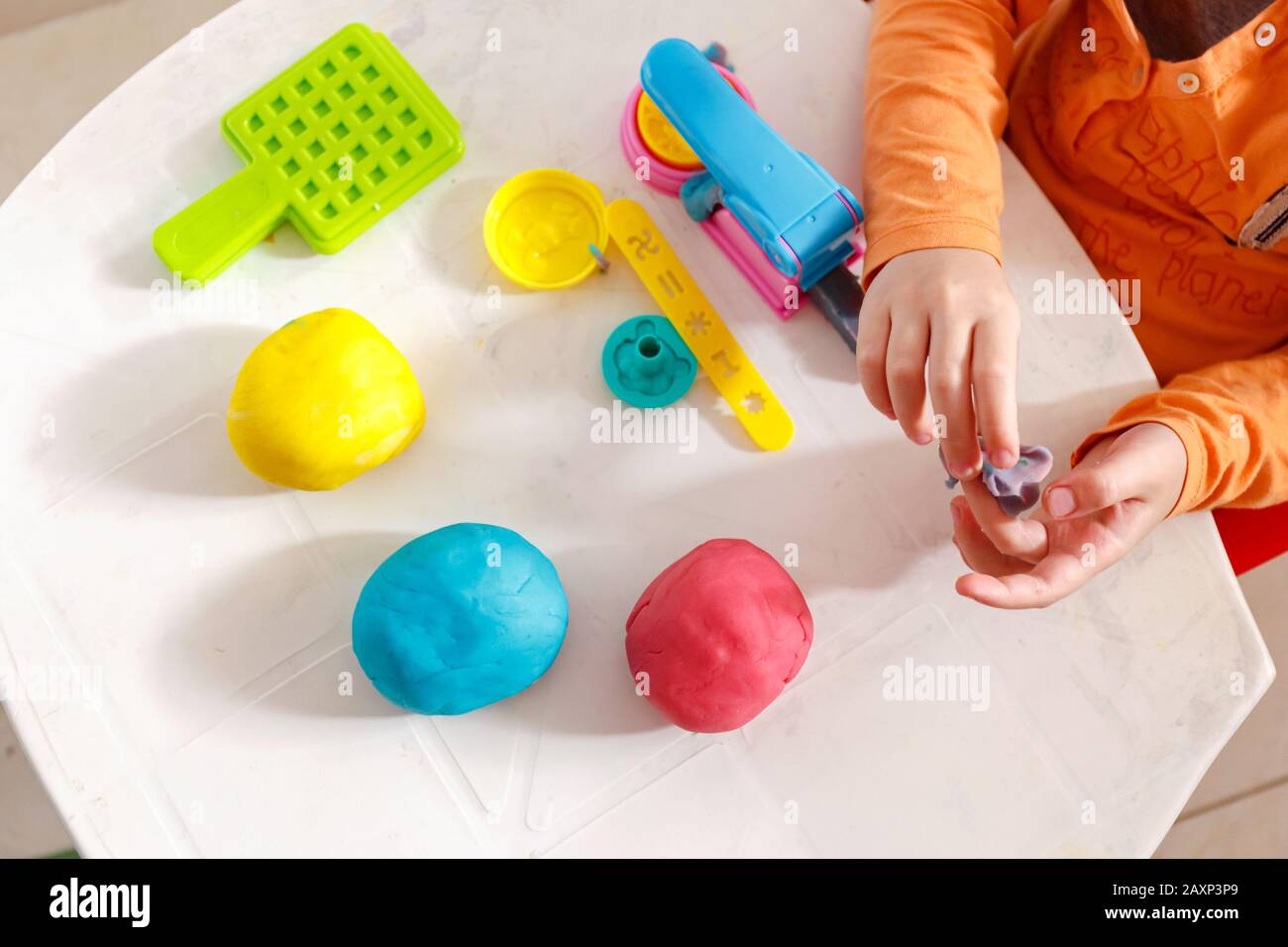 child playing a home made playdough. Yellow, orande and pink modelling
