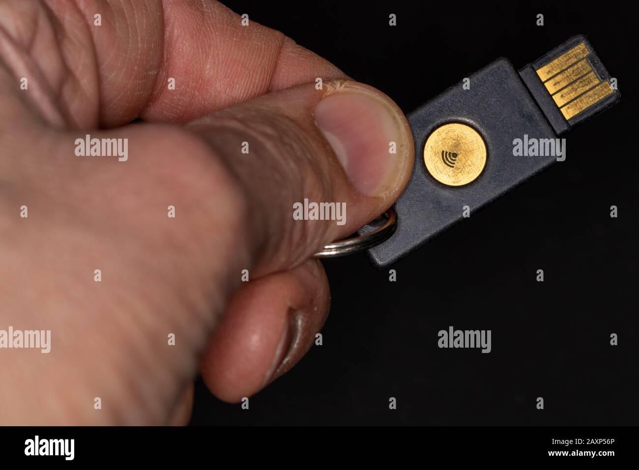 Hand holding hardware security key for use with laptop or computer to