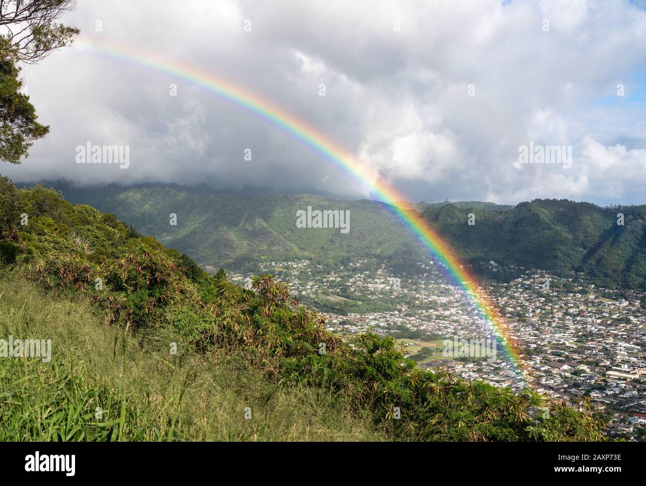 Bright rainbow over the suburbs of Woodlawn and Manoa in a valley above Honolulu on Hawaii Stock Photo