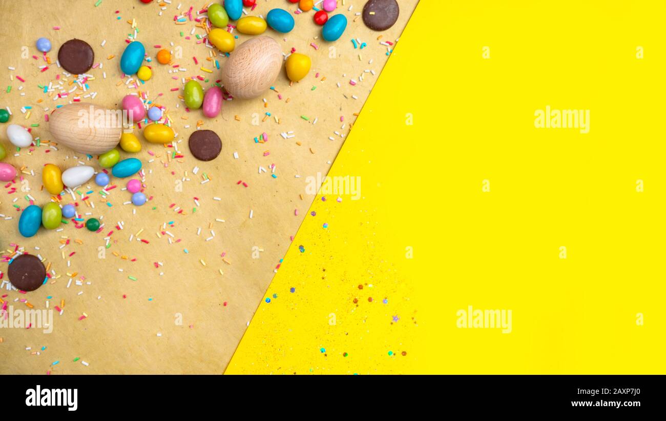 Wooden Easter eggs, sweets on yellow background, copy space Stock Photo