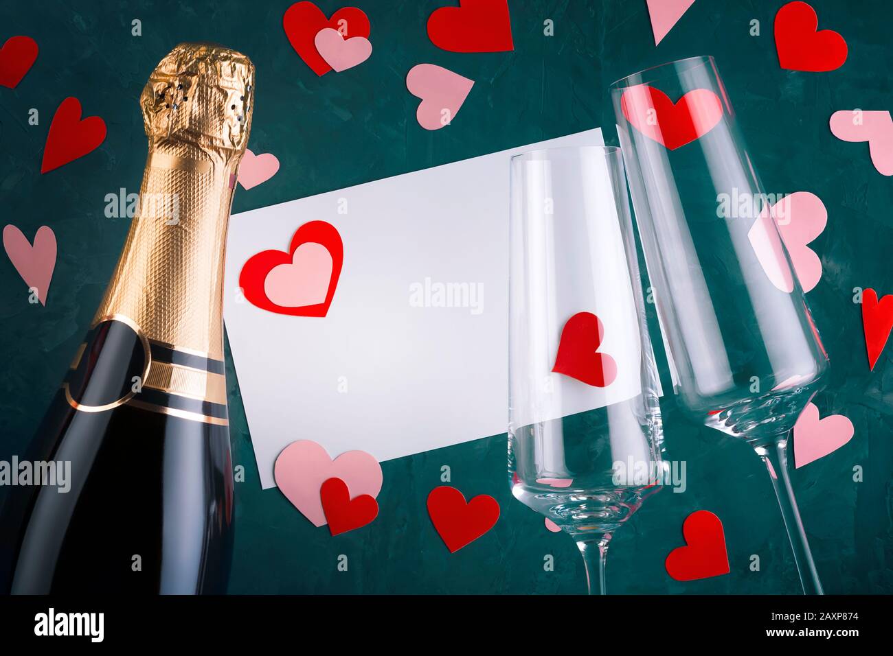 Valentine's day greeting card with bottle of champagne, two elegant luxury glasses, scattered hearts of various shapes cut out of paper with copy spac Stock Photo