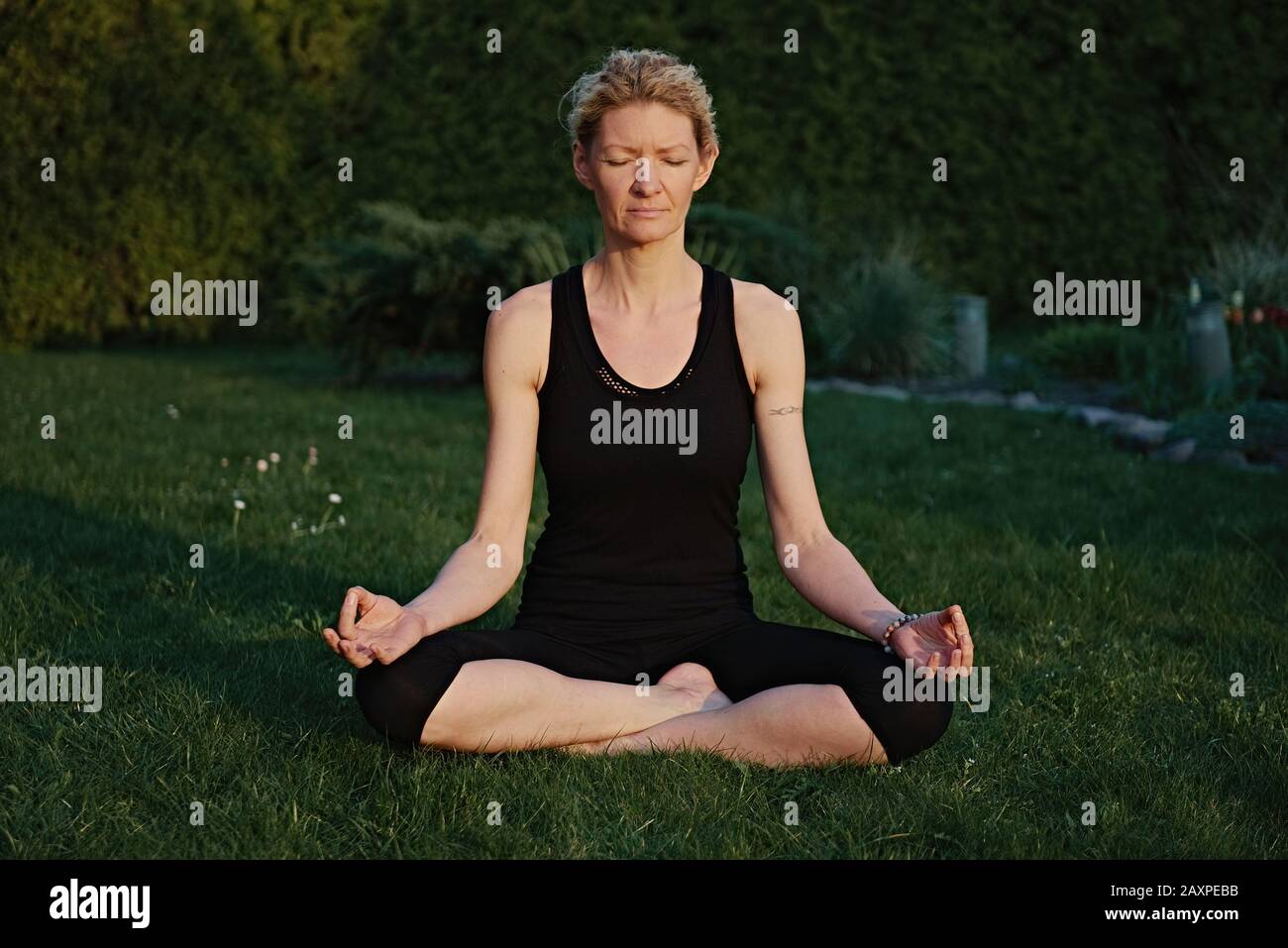 Young woman doing yoga in meditation posture on a mat in the garden. Stock Photo