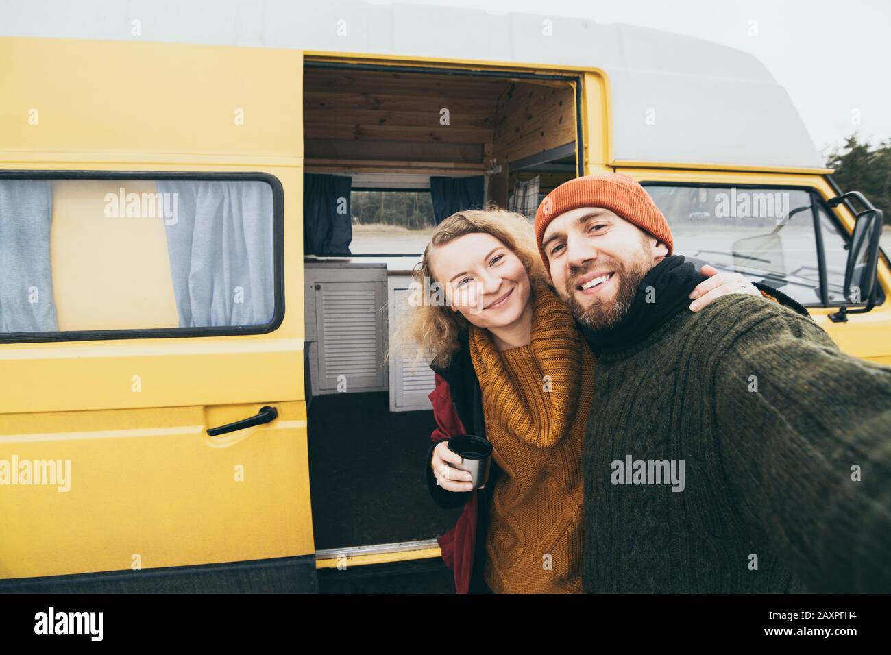 Young happy couple taking selfie in front of their yellow camper van Stock Photo