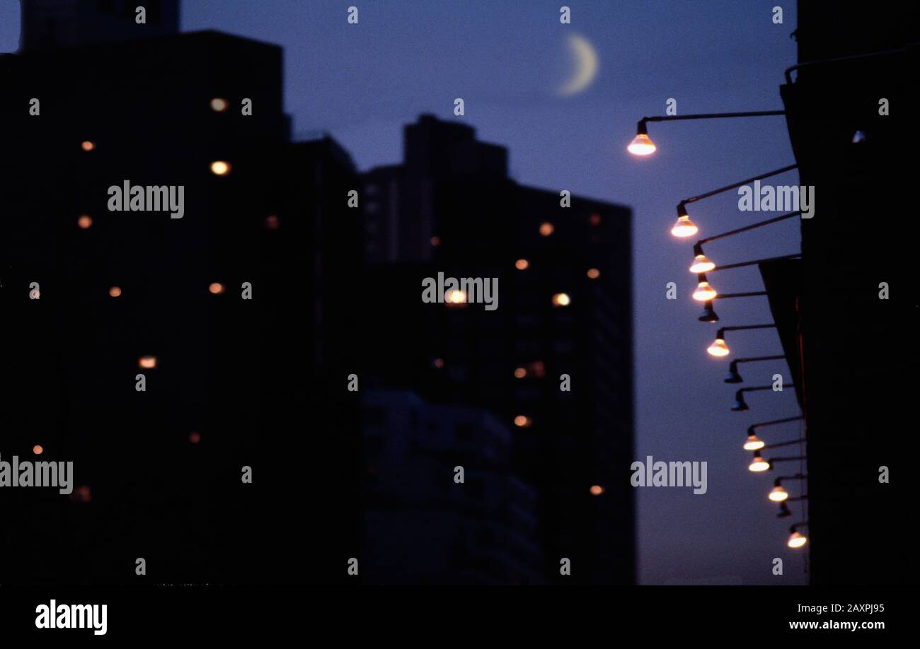 Nighttime scene with crescent moon, apartment buildings and street lights Stock Photo
