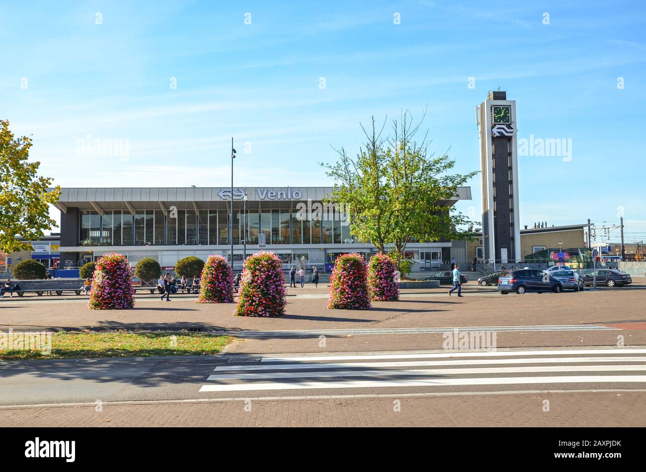 Venlo, Limburg, Netherlands - October 13, 2018: Zebra crossing and sidewalk leading to the main train station building in the Dutch city. Flower decorations, parked cars, people on the street. Stock Photo