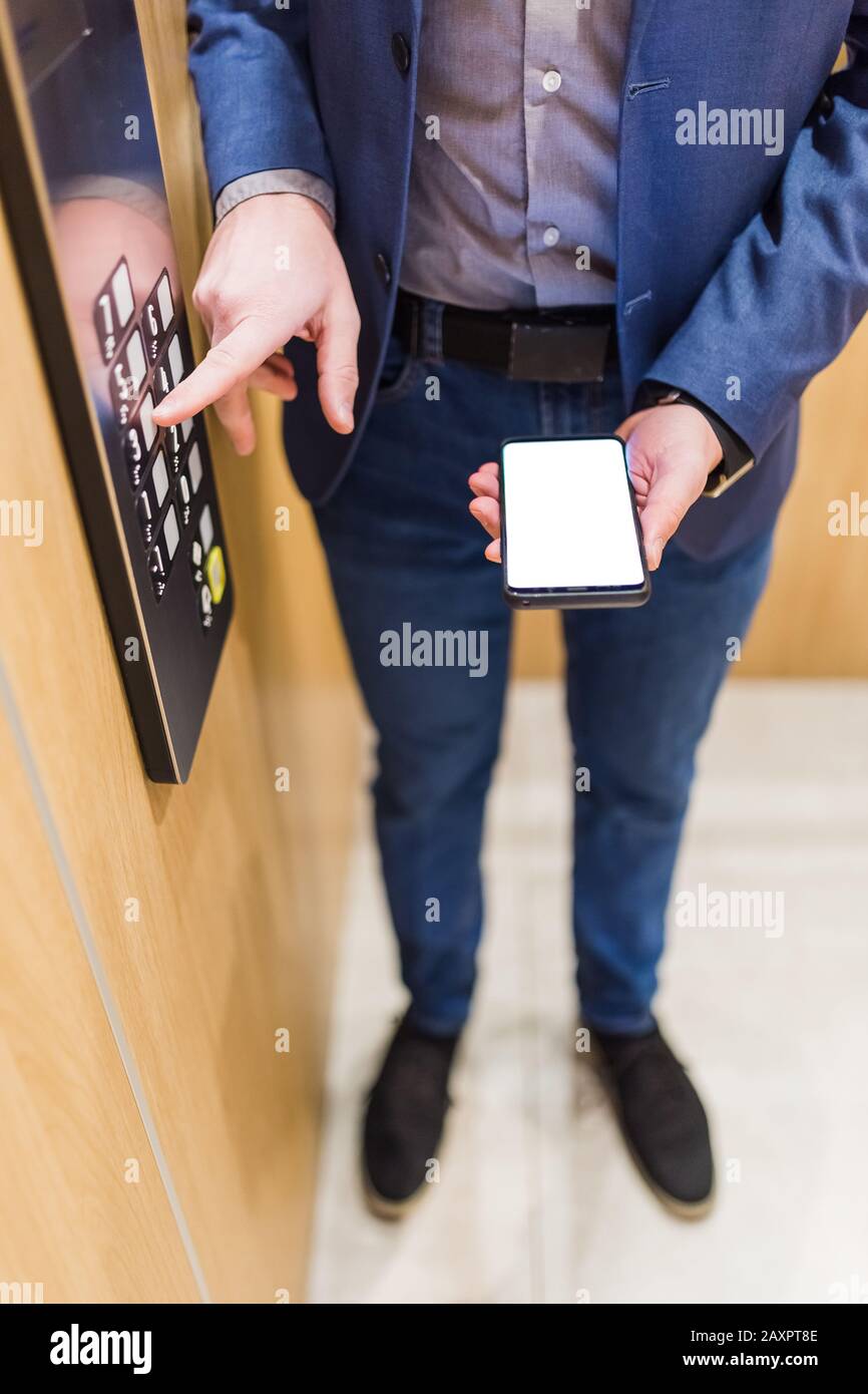 Man hands holding blank screen mobile phone while using elevator control panel. Stock Photo