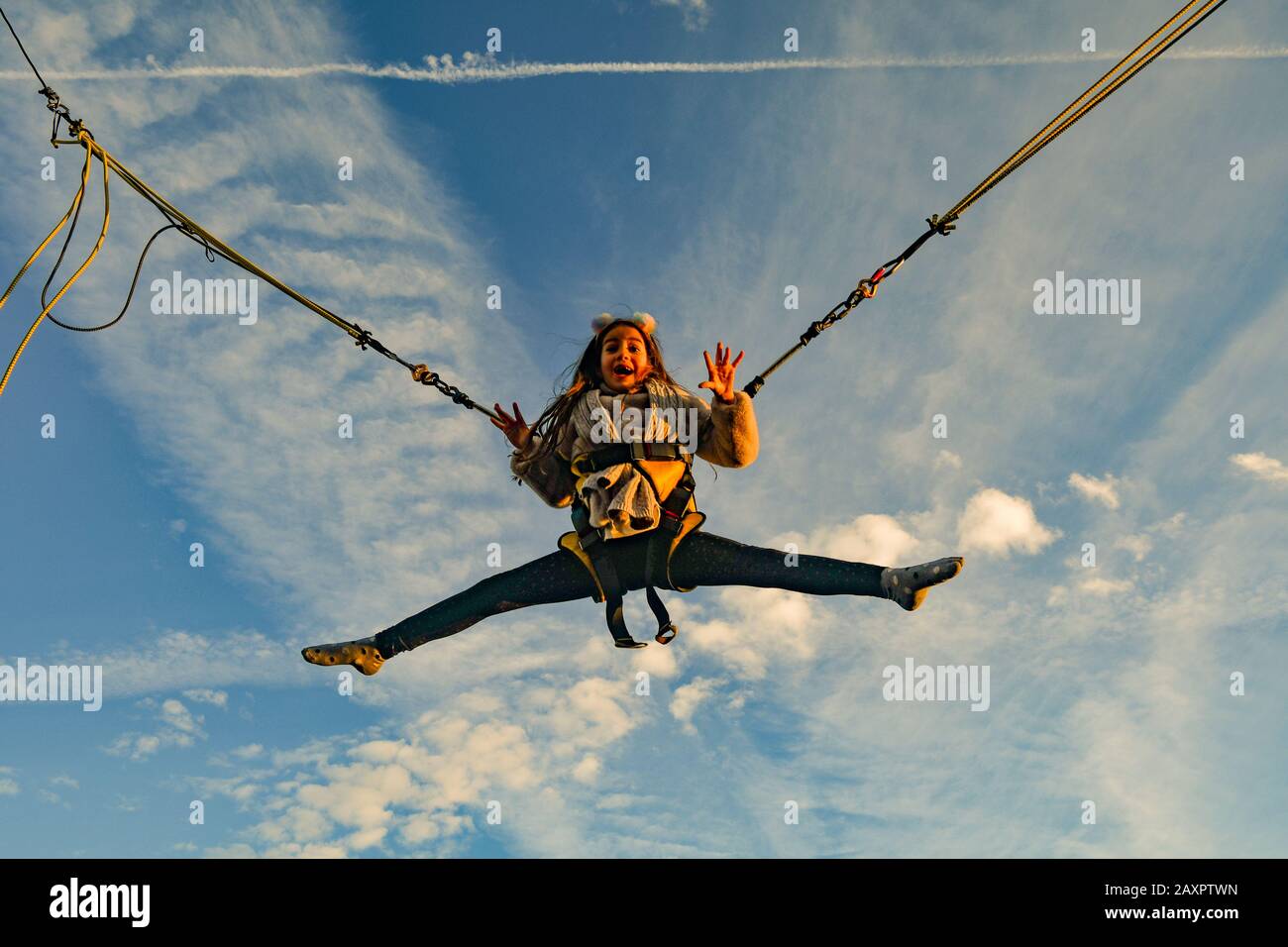 A smiling little girl (9 years old) suspended in the air jumping on a trampoline with clear blue sky background, Italy Stock Photo