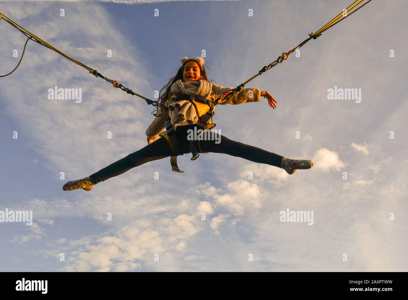 A smiling little girl (9 years old) suspended in the air jumping on a trampoline with clear blue sky background, Italy Stock Photo