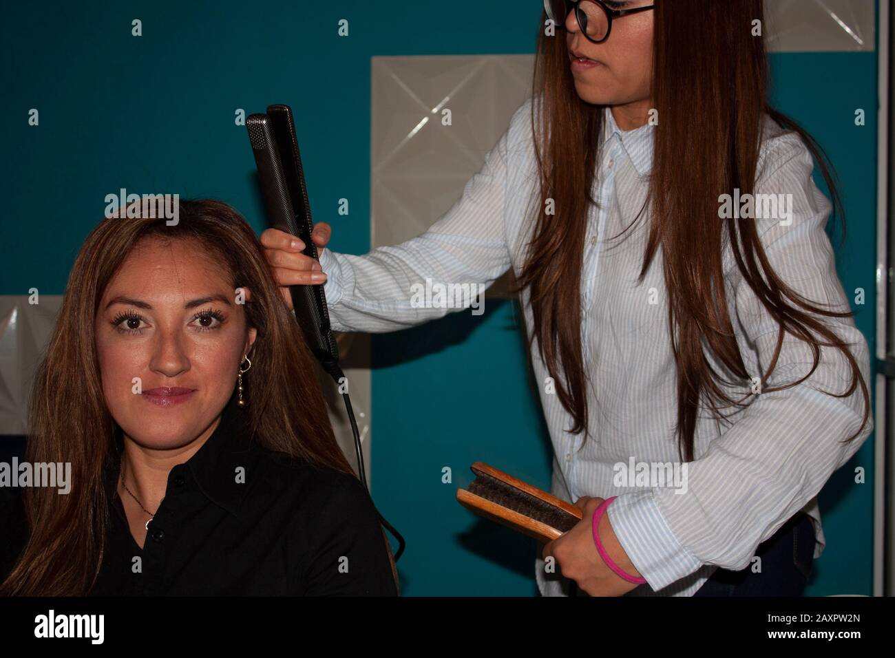 Latin American brunette women beautifying and combing hair in Mexico using brush and ironing tongs Stock Photo